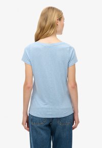 Lichtblauw T-shirt met korte mouwen en een ronde halslijn, zachte textuur en een rechte snit. De achterkant heeft een centraal naaddetail. Dit is gecombineerd met losse denim.