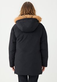 Czarna parka z odpinanym kapturem wyłożonym futrem. Gładka faktura, średnia długość, długie rękawy i boczne zamki do regulacji.