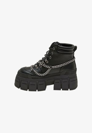 Masywne czarne buty wojskowe z wysoką cholewką, sznurowane z przodu, z akcentem w postaci srebrnego łańcucha oraz grubą, teksturowaną gumową podeszwą. Wykonane ze skóry.