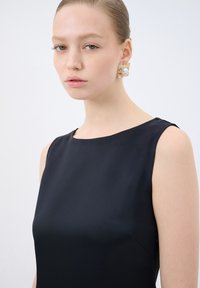 Robe noire sans manches en tissu lisse et avec un col rond. Boucle d'oreille dorée remarquable avec un détail en perle. Design simple et élégant.