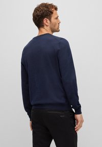 Navy blue sweater in a lightweight knit, featuring a crew neck and ribbed cuff. Paired with black pants displaying a discreet brand logo.