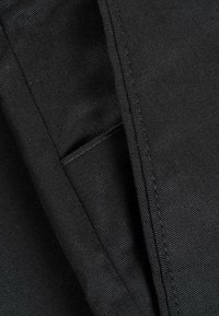 Black fabric with a textured weave, featuring stitched seams and a small pocket detail, creating a layered appearance.