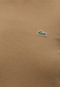 Tissu beige texturé avec un petit logo crocodile vert brodé sur le côté droit.