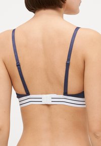 Marineblauwe bralette met dunne, verstelbare bandjes. Voorzien van een witte band met zwarte strepen voor ondersteuning. Glad stoftextuur.