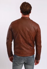 Braune Lederjacke mit strukturierten Nähten, hohem Kragen und Reißverschlussärmeln. Über blaue Jeans getragen, von hinten betrachtet.