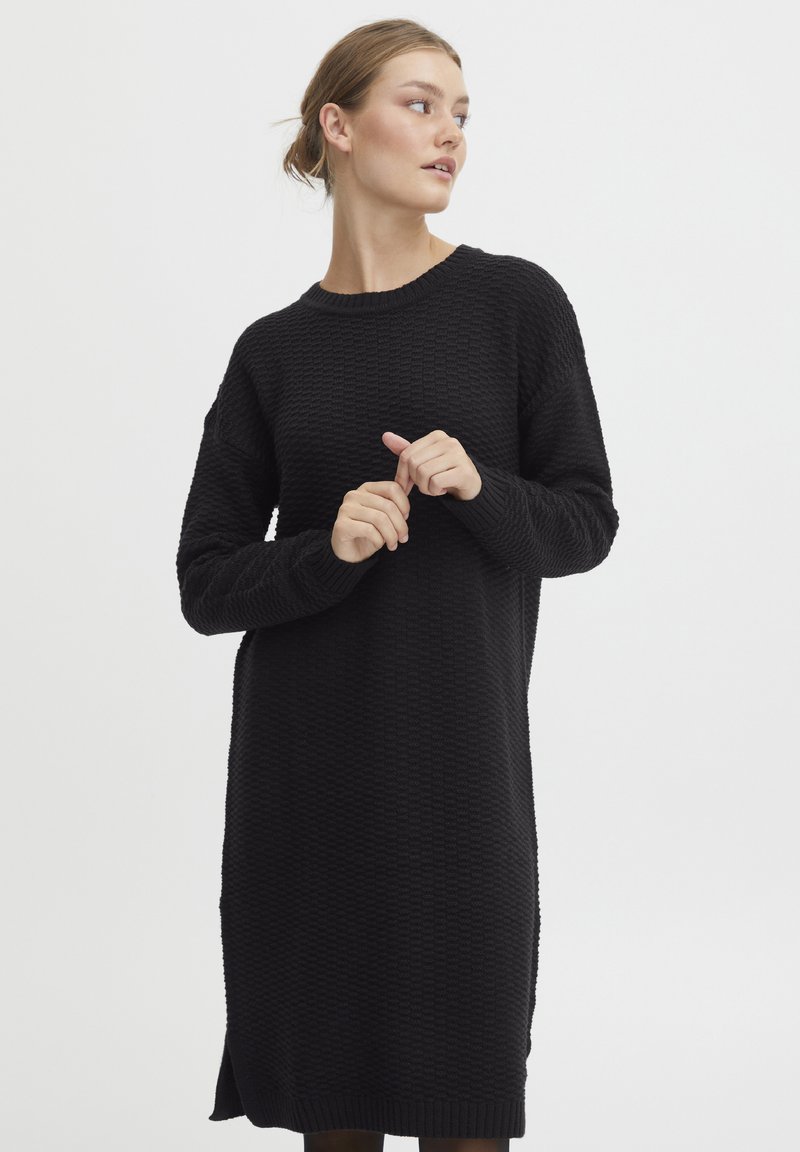 Abito nero a maglia con un motivo testurizzato, scollo a girocollo e maniche lunghe con fessure laterali all'orlo. Vestibilità morbida e rilassata.
