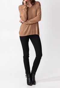 Vaaleanruskea pitkähihaisen V-aukkoinen paita yhdistettynä mustiin kapealahkeisiin farkkuihin ja mustiin nilkkureihin. Pehmeä kangas, rento istuvuus; sileä pinta.