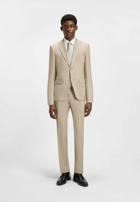 Beige skræddersyet jakkesæt i slim fit, med notch lapels, to frontlommer og et tekstureret slips. Båret med sorte sko.
