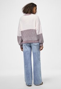 Pullover lavorato a maglia, oversize bicolore in rosa e viola con una texture a coste. Abbinato a jeans blu a vita alta e gamba larga.