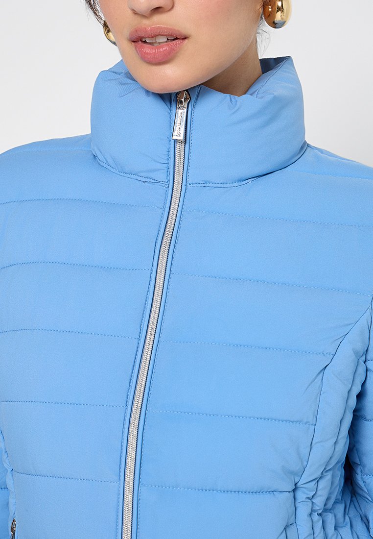 Hellblauer Pufferjacke mit hohem Kragen, vertikalen Nähten und einem Reißverschluss auf der Vorderseite. Sie verfügt über eine weiche, glatte Textur und eine taillierte Passform.