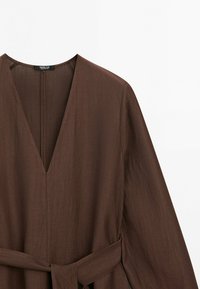 Robe marron à manches longues avec un décolleté en V profond et une ceinture en tissu assorti nouée à la taille.