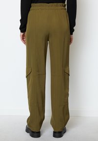 Olivově zelené cargo kalhoty s volným střihem, elastickým pasem, bočními kapsami a hladkým povrchem. Černé platformové boty viditelné u nohou.