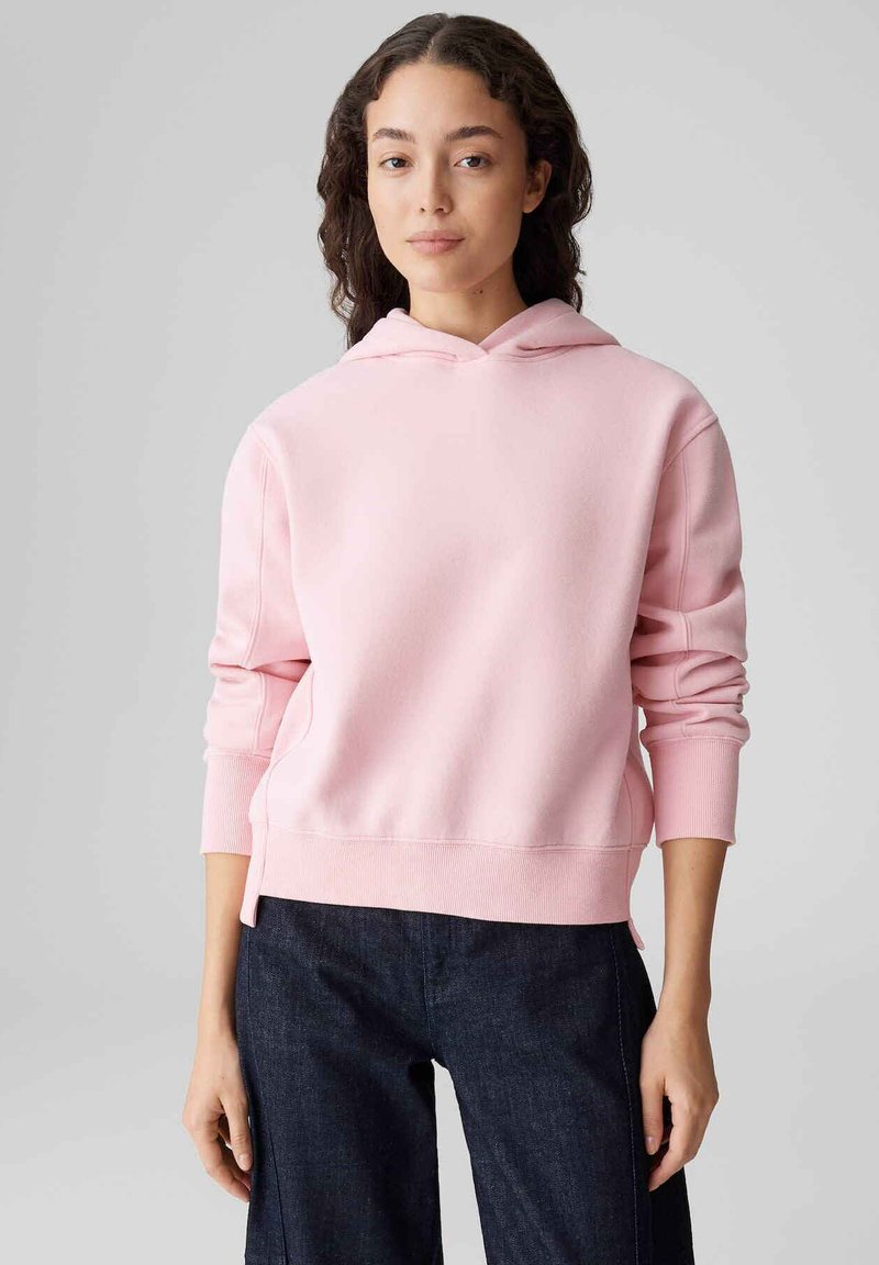 Felpa con cappuccio color rosa chiaro con polsini e orlo a costine, caratterizzata da una vestibilità comoda. Abbinata a pantaloni in denim scuro, con texture liscia in cotone.