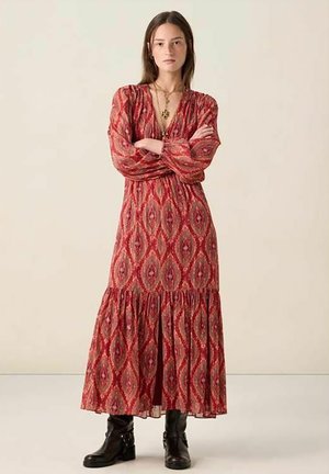 Robe rouge à manches longues avec un corsage cintré, un décolleté en V, un ourlet à volants et un motif complexe en losanges. Portée avec des bottines noires.