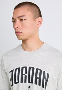 Grå bomulds T-shirt med stort "JORDAN" print i sort med hvid kant, rund halsudskæring og korte ærmer.