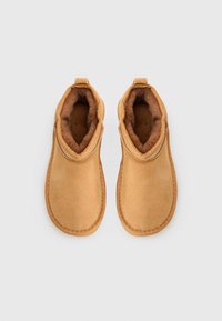 Botas de tobillo de ante marrón con suave forro de piel de color marrón. El diseño incluye una cinta en la parte superior para facilitar el uso y bordes cosidos para mayor durabilidad.