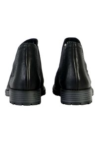 Zapatos de cuero negro con textura lisa, diseño de punta redondeada y suelas de goma a rayas, vistos desde la parte trasera.