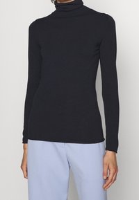 Schwarzes Rollkragenoberteil mit langen Ärmeln, figurbetontem Design, weicher Textur und minimalen Details. Kombiniert mit hellblauen Hosen.