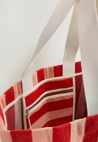 Torebka materiałowa w paski w odcieniach czerwieni i różu, z kremowymi uchwytami oraz wewnętrzną kieszenią na zamek dla bezpiecznego przechowywania.