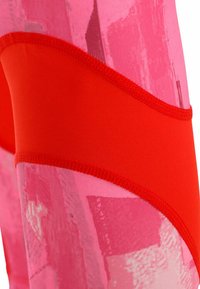 Leggings de alto rendimiento con un tejido texturizado rosa y patrones abstractos, realzados por paneles rojos sólidos y costuras en contraste.