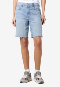Bermuda in denim azzurro con vestibilità comoda, orlo sfrangiato, design a cinque tasche e chiusura con bottone. Abbinati a sneakers grigie e viola.