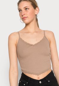 Top cropped em material canelado castanho claro com rendas ao longo da gola e do final, apresentando alças finas ajustáveis.