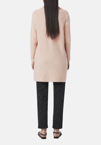Light pink long-sleeve knit top with a straight cut, paired with black pants featuring a textured zigzag pattern and flat sandals.
