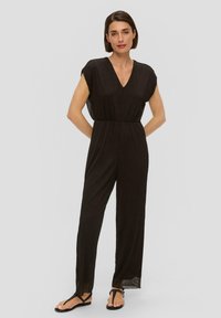 Zwarte, mouwloze jumpsuit met een V-hals, met een taillering en wijde benen. Gemaakt van een gestructureerde stof met doorzichtige zijpanelen.
