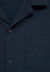 Marineblaues Hemd mit strukturiertem Stoff, einem Reverskragen und einer aufgesetzten Tasche. Verfügt über eine vordere Knopfleiste und ein dezentes Rippmuster.