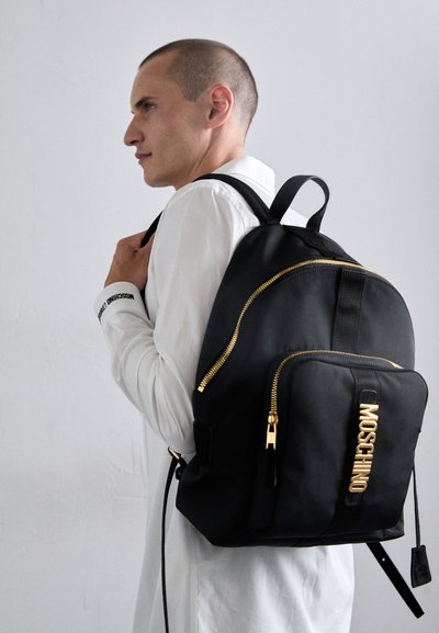 Rucsac negru din nailon cu fermoare aurii, buzunar frontal și logo embosat. Formă rotunjită cu bretele ajustabile și mână superioară.