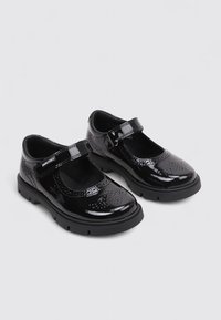 Zapatos Mary Jane de charol negro con detalles perforados, cinta de cierre de gancho y bucle, y suelas de goma gruesa, diseñados para niños.