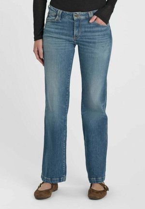Donna che indossa jeans a gamba dritta di lavaggio medio con tasche frontali, abbinati a ballerine marroni e una maglia nera a maniche lunghe.