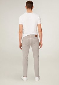 Pantalones de hombre en gris claro, corte slim, fabricados en algodón, con diseño de cinco bolsillos y un parche de cuero marrón en la cinturilla.