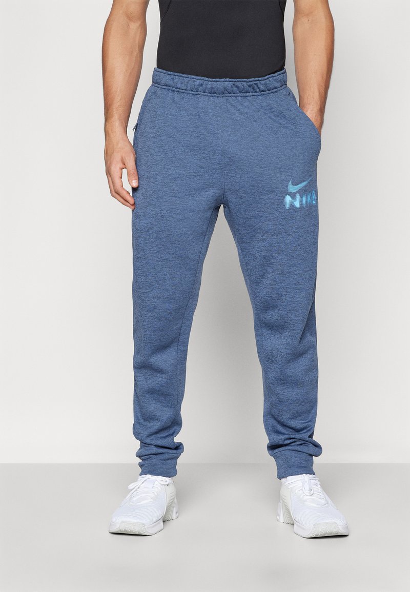 Blå atletiske sweatpants med elastisk taljebånd, sidelommer og et reflekterende Nike-logo trykt på den øverste venstre lår. Blød tekstur.