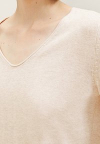 Beiger V-Ausschnitt-Pullover aus weichem Strickmaterial; verfügt über ein strukturiertes Muster entlang der Schulternaht und einen dezenten Glanz.