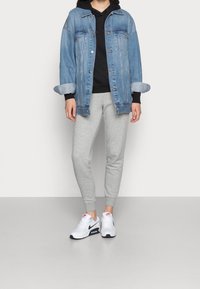 Lichte blauwe spijkerjack, zwarte hoodie eronder, grijze joggingsbroek en witte sneakers met rode en marineblauwe accenten. Opgerolde mouwen van het jack.