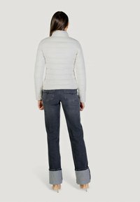 Giacca a piumino leggera color panna con colletto alto, caratterizzata da un design trapuntato orizzontale. Abbinata a jeans scuri con risvolti.