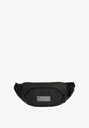 Čierny ľadvinka vyrobený z nylónu, s predným zipsovým vreckom, nastaviteľným popruhom a obdĺžnikovou sivou etiketou s textom.