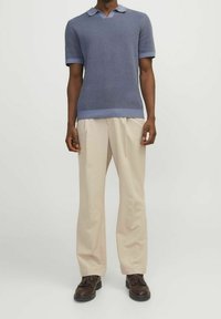 Pletená polokošile s krátkým rukávem v světle modré barvě, s výstřihem do V a kontrastním lemem. Spárována s béžovými kalhotami s širokými nohavicemi a tmavě hnědými botami.