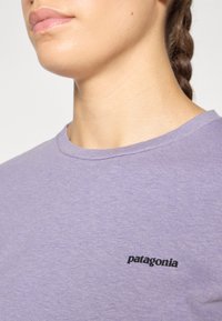 T-shirt en coton violet avec un col rond et un logo "Patagonia" noir imprimé sur la zone gauche de la poitrine. Texture douce.