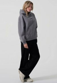 Grå oversized hettegenser med frontlomme og snorhette, sammen med svarte vide bukser og lyse sneakers.