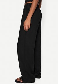 Wide-leg black pants made of lightweight fabric, featuring an elastic waistband and side pockets, paired with flat black sandals.