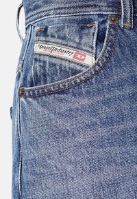 Jeans de denim con un lavado azul claro, con una etiqueta de Diesel Industry en un bolsillo trasero, remaches de cobre y costuras en contraste.