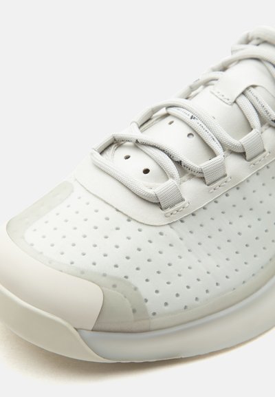Κοντινή λήψη ενός λευκού δαχτύλου sneaker με διάτρητο ύφασμα, ενισχυμένη άκρη και χοντρές λευκές κορδόνια περασμένες μέσα από υφασμάτινους βρόχους.