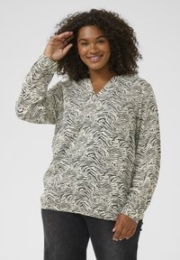 Kreklu piedurkņu blūze ar krēmkrāsas un melnu zebru rakstu, ar V-veida kakla izgriezumu un br�īvu piegriezumu, izgatavota no mīksta, teksturēta auduma.