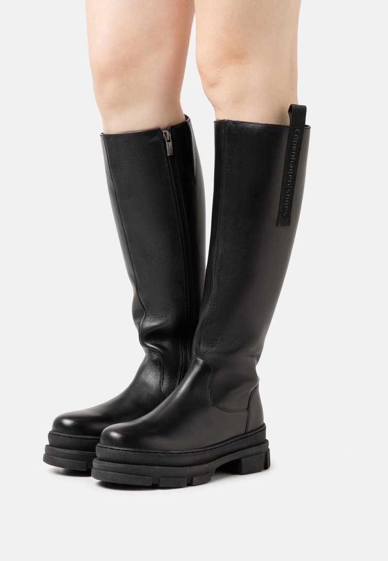 Černé kožené vysoké boty až ke kolenům s masivní platformou, bočním zipem a smyčkovým označením pro snadné nazouvání. Hladká textura a elegantní design.