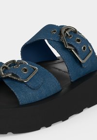 Μπλε υφασμάτινο σανδάλι με δύο ρυθμιζόμενους ιμάντες με ασημένιες μεταλλικές αγκράφες και παχιά μαύρη σόλα.