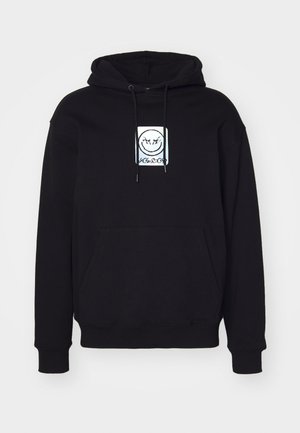 Hoodie noir en tissu doux, avec un graphisme centré représentant un visage souriant. Il est équipé d'une poche avant et d'une capuche réglable avec cordon.