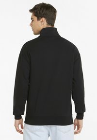 Maglione nero con colletto alto, polsini a coste e tessuto strutturato. Presenta una vestibilità rilassata e un colore uniforme senza motivi o accenti.