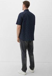 Camicia a maniche corte blu navy con piccoli motivi bianchi, in tessuto di cotone, colletto button-down, abbinata a jeans grigio scuro e sneakers bianche.